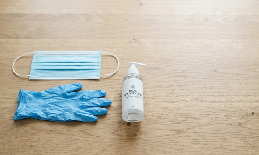 Einwegmaske, Pflegehandschuhe und Handdesinfektionsmittel ordentlich auf einem Holztisch arrangiert.